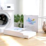 Kobieta trzyma białą bluzkę zafarbowaną na różowo obok otwartej pralki